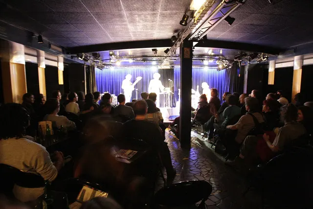 Public assis devant la scène éclairée d'une petite salle de spectacle