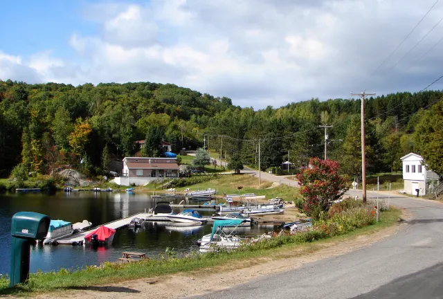 Quai et bateaux sur le lac Papineau au hameau de Vernet, avec des maisons et une colline boisée