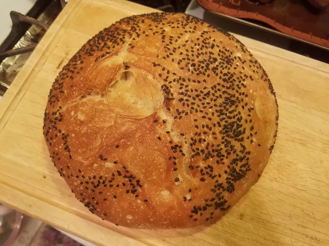 Miche de pain au levain parsemée de graines de pavot, sur une planche de bois