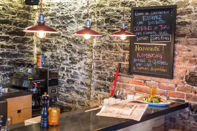 Salle de restaurant aux murs de pierre avec tableau noir et lampes suspendues, dans le Vieux-Québec