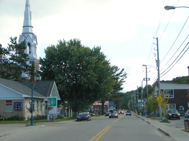 Rue principale de Chénéville avec commerces, voitures et le clocher de l'église