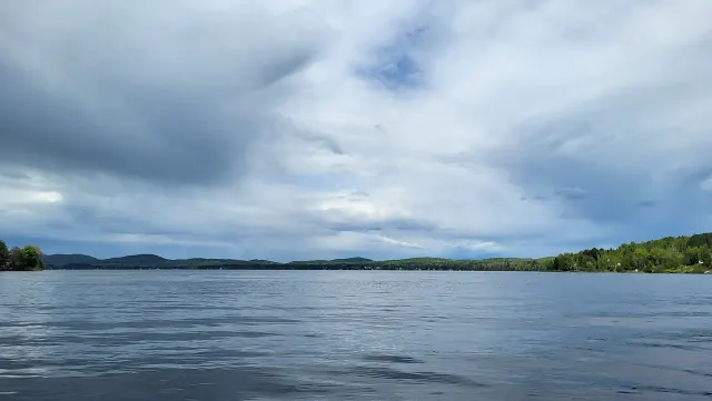 Le lac des Plages sous un ciel nuageux de mai, avec une rive boisée au loin