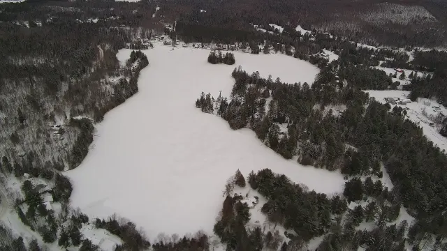 Vue aérienne du lac Lévesque gelé et enneigé, entouré de forêt, en janvier