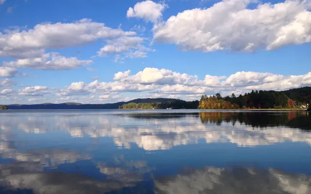 Nuages blancs reflétés dans le lac Simon, rive aux couleurs d'automne