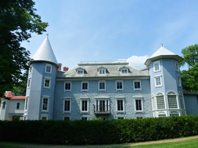 Façade gris-bleu du manoir Papineau entre ses deux tours, derrière une haie