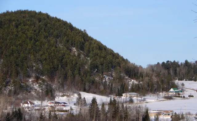 Colline boisée au-dessus des maisons de Notre-Dame-de-la-Salette, champs enneigés