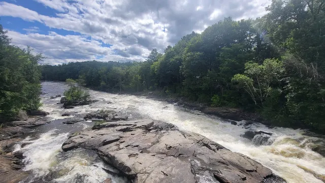 Rapides des chutes du Moulin sur de larges dalles de roc, sous un ciel nuageux